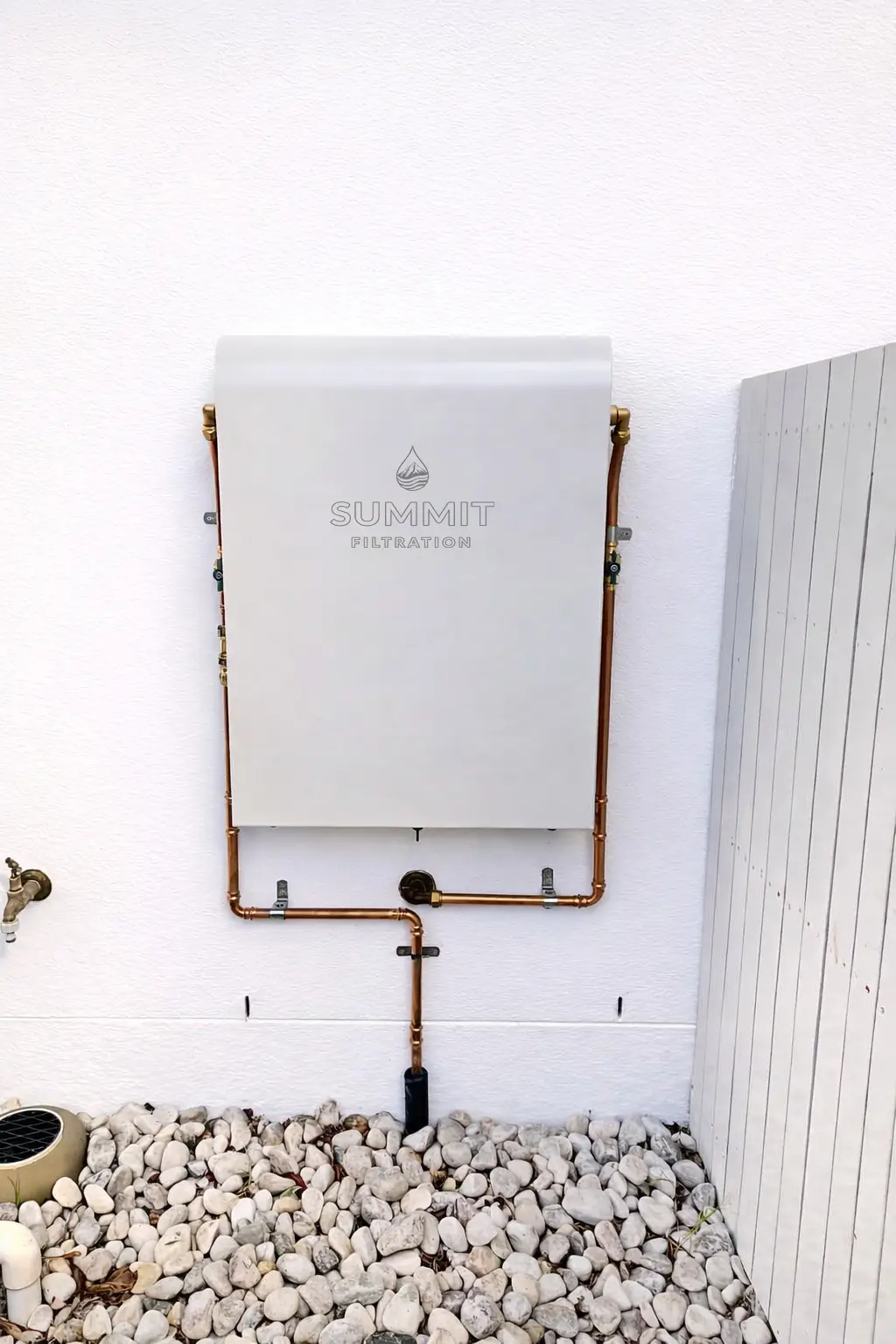 White whole house water filtration system installed on modern rendered wall with copper pipework.